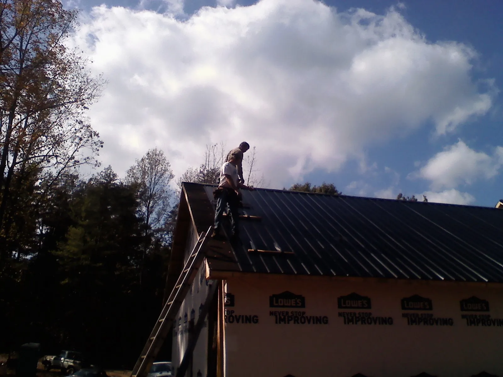 Roofer fastening dark metal panels high against a cloudy sky, from a Roof Inspection job in Durango