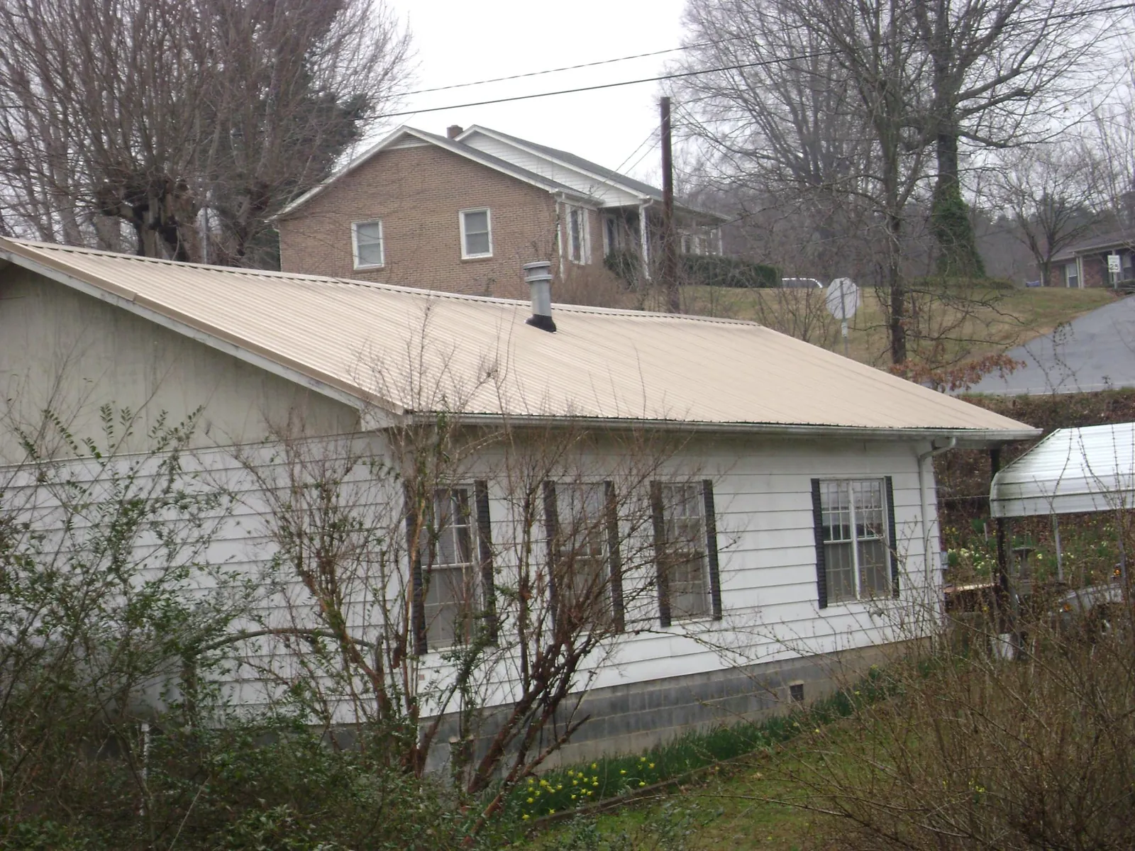 Tan metal roof on a white sided house set into a hillside — Commercial Roofing by Roofing Brothers in Durango
